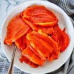 Roasted capsicums in white bowl with fork.