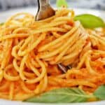 Fork being twirled in plate of pasta with basil leaves on top.