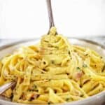 Fork being twirled in grey bowl of fettuccine pasta.