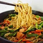 Chop Sticks holding noodles above salmon and vegetable stir fry