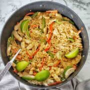 Cooked satay chicken noodles in large black pan with silver spoon.
