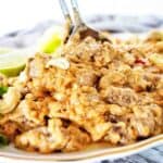 Lamb satay on white plate with cashews and serving spoons.