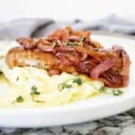 Sausages with caramelised onions on white plate with mashed potatoes.