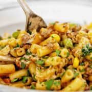 Fork in bowl of beef mince pasta with parsley on top.