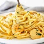 Fork being twirled in pasta with scallops on white plate.