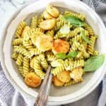 Pesto pasta with scallops in grey bowl with fork and spoon.