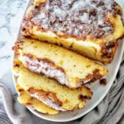 Apple cake topped with vanilla glaze sliced into pieces on white serving platter.