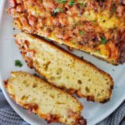 Slices of cheese bacon bread with remaining loaf on white plate.