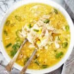 Chicken and corn soup in white bowl with spoon and fork.