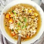 Chicken soup in a white bowl with fork and spoon.