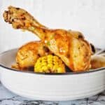 Chicken leg with gravy in white bowl with corn cobs.