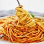 Fork being twirled in spaghetti on white plate.