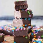 Pieces of chocolate fudge with colourful sprinkles stacked on marble surface.