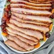 Slices of glazes ham on serving platter with cherries and apricots.