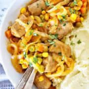 Curried sausages with vegetables and mashed potato in white bowl.