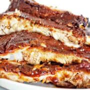 Slow cooker dry rub ribs stacked on white plate.