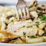 Fork pushed into chicken on white plate with mashed potatoes.