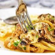 Fork being pushed into meatball with cheese on white plate.