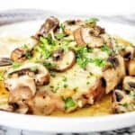 Cooked pork chop on white plate with mushrooms and melted cheese.