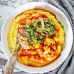 Osso bucco in white bowl with polenta and gremolata.