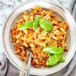 Pasta with meat sauce in grey bowl with basil leaves on top.