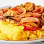 Sausage and peppers with polenta on white plate.