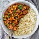 Savoury mince with rice in a white bowl with fork and spoon.