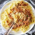 Slow Cooker Spaghetti Bolognese on white plate with fork and spoon in the middle