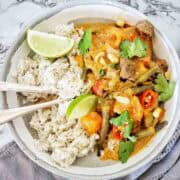 Thai Red Curry With Beef in grey bowl with rice and lime wedges.