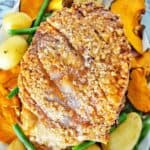 Roast pork and crackling on white plate with vegetables.