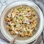 Risotto with steak pieces in a grey bowl with fork and spoon.