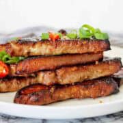 Pork rashers on white plate with green onions and chilli slices.