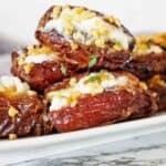 Stuffed dates with goat cheese and nuts on white background with thyme leaves on top.