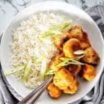 Sweet and sour pork meatballs in white bowl with rice.