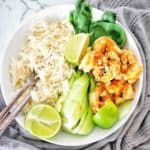 Prawns in white bowl with rice and lime wedges.