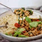 Spool holding basil pork over bowl of the same with fried egg and rice.