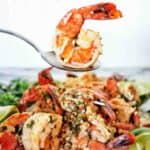 Spoon holding cooked prawn above white plate of the same.