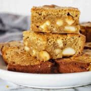 Blondies with nuts and chocolate stacked on white plate.