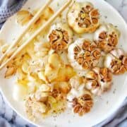 Whole roasted garlic on white plate with garlic skin and pair of wooden tongs