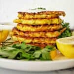 Stack of fritters on white plate with lemon, parsely and sauce.